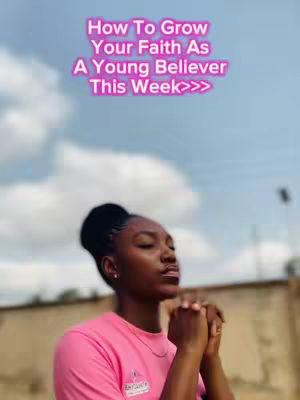 A young woman in a pink shirt is positioned in front of a slightly blurred background of sky and building outlines. Her hands are clasped together in a prayerful pose. Above her, overlaid text in a pink gradient, reads 'How To Grow Your Faith As A Young Believer This Week>>>'.