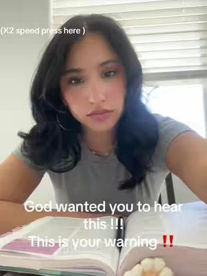 A young woman with long, dark hair is centered in a selfie-style shot, looking slightly down at an open Bible in front of her. She appears to be in a room with a window visible in the background. Text overlays are added to the image.