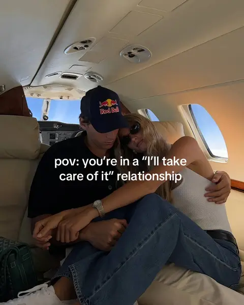 The cover image captures a couple embracing inside a private jet. The man, wearing a dark blue baseball cap with a Red Bull logo, is leaning his head toward the woman. The woman, wearing sunglasses and a white tank top, is nestled against him. The interior of the jet showcases cream-colored seating and an overhead view of the cabin. The couple is positioned close together, hinting at a moment of intimacy and comfort.
