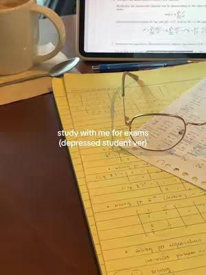 A close-up shot of a desk with study materials. Yellow legal pads are in the foreground with handwritten notes. A pair of glasses is resting on one of the pads. To the left is a white mug and a stack of books. A tablet displaying a screen with equations is in the background, along with a pen. The lighting is soft, and the scene suggests a study environment.