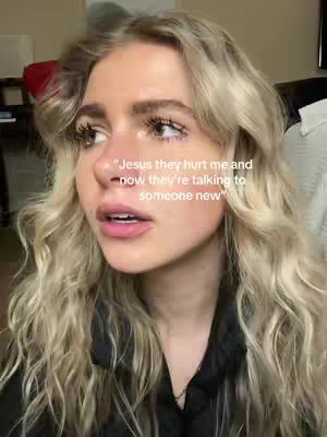 A selfie-style shot focuses on a woman's face, with long wavy blonde hair and a black top. The background is blurred but suggests an indoor setting. overlaid text above reading, Jesus they hurt me and now they're talking to someone new.