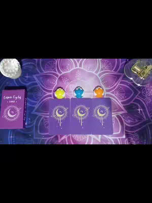The cover image features a purple background with a mandala design. Three tarot cards face up in the center, each with a crescent moon and star design. Above the cards are three small figurines–yellow, blue, and orange. To the left of the cards is a purple book titled 'Cosmic Eye by Tarot'. To the upper right is a glass dish with a gold item and in the upper left a similar dish with a white substance. The overall composition is symmetrical and mystical, with bright colors.