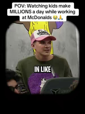A man is centered in the frame, wearing a pink-and-white baseball cap and a green crewneck shirt. Above him, text in a white box reads, 'POV: Watching kids make MILLIONS a day while working at McDonalds' with a thinking emoji and praying hands emoji. The background is blurred, possibly showing a person wearing a yellow shirt or top. In the foreground, a dark screen and some of the man's shirt and a purple sweatshirt is visible. Below the text, the words 'IN LIKE' appear in a white box. The overall composition is casual, capturing a moment in the social media style.