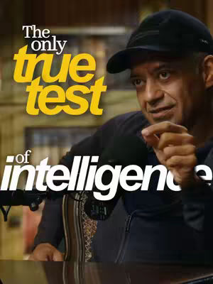 A man wearing a black baseball cap and a dark jacket is looking towards the right, holding a microphone. Overlayed on the image is a block of yellow text that reads 'The only true test', and the rest of the phrase, 'of intelligence' is in white text below it.