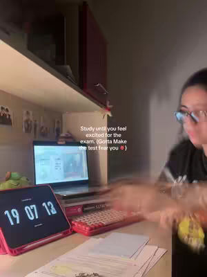 A person is sitting at a desk with a laptop, tablet, and a red keyboard. The room has a shelf with some decorations. There is a text overlay on the image.
