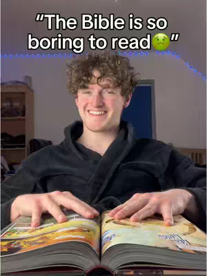A young man with curly brown hair, wearing a black robe, sits with open hands over an open book. The book's pages show colorful illustrations. Text overlayed on the image reads "The Bible is so boring to read" with a green, sad-face emoji. The background features a room with warm lighting and a shelf.