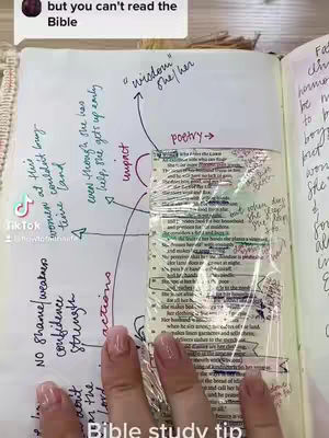An open Bible with handwritten notes around a passage. The image is dominated by the open book, with handwritten annotations in pen and highlighter surrounding a section of the text. The lower part of the frame shows a hand with long, manicured nails, holding a piece of clear plastic over the Bible page.