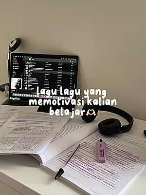 The image shows a workspace with a laptop displaying a playlist, open books with handwritten notes, a pen, a purple USB drive, and headphones. The text overlay reads, 'Lagu lagu yang memotivasi kalian belajar' (Songs that motivate you to study). The overall composition suggests a study-focused aesthetic with soft lighting.