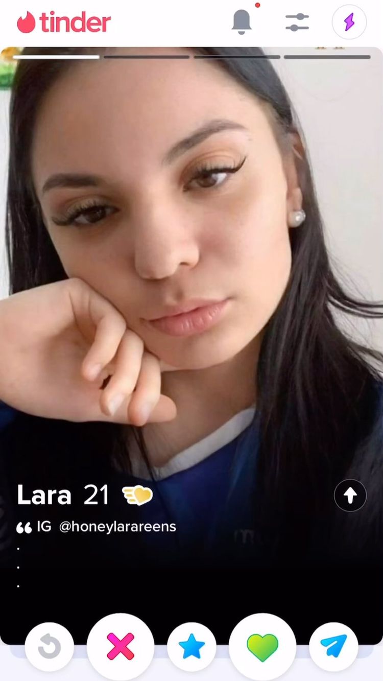 A Tinder profile screenshot featuring a young woman with dark hair and fair skin. She rests her head on her hand, looking at the camera with a slight pout. The Tinder interface is visible with her age and name displayed, as well as social media details and a selection of app icons.