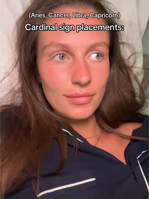 A selfie-style shot with a woman lying in bed, looking towards the right. The background is a soft, white sheet. The woman has long brown hair, and is wearing a dark blue top with white trim. Text overlays at the top say '(Aries, Cancer, Libra, Capricorn)' and 'Cardinal sign placements:' in white font.