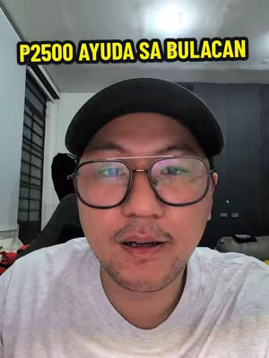 A man wearing glasses and a black cap is centered in the frame, with text overlayed above his head. The background is a blurred interior.