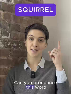 A woman with short dark hair stands in front of a brick wall. She smiles and points her right index finger upwards. A purple rectangle above her head reads the word 'SQUIRREL' in white font, and overlaid text at the bottom says 'Can you pronounce this word'. The overall lighting is bright, and the composition focuses on the woman's upper body.
