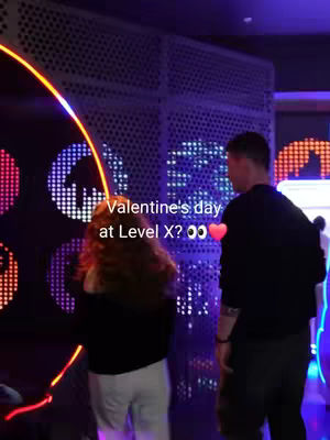 A dimly lit shot shows a couple standing in front of a wall with illuminated circular designs. Text overlayed on the image reads, "Valentine's day at Level X?" with heart and eyes emojis.