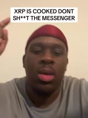 A close-up shot of a Black man pointing upwards. He is wearing a red durag and a grey shirt, and the background is a plain wall.