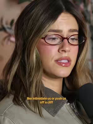 A woman with long, light brown hair and glasses is shown in a close-up shot, speaking with a concerned expression. Text is overlaid near her jaw.