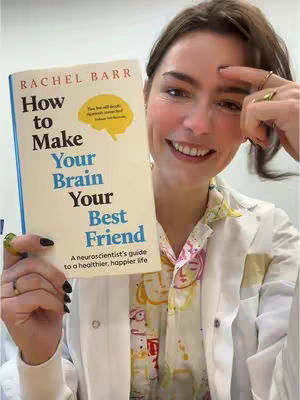 A woman is holding a book titled "How to Make Your Brain Your Best Friend" with the author's name at the top. She is smiling at the camera, with one hand on her face.