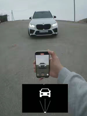 An overhead shot featuring a white car driving towards the camera on a grey road. Below the car, a person is holding a phone displaying the car. Underneath the phone is a graphic of a car icon with converging lines and a dot at the bottom.