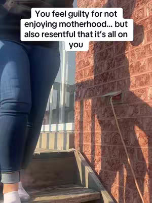A person's legs and lower body are visible in the image; the person is wearing dark jeans and white shoes, resting on the stairs. The setting includes a brick wall and a window.