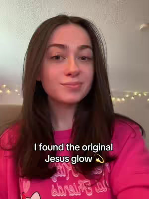 A woman with long, dark hair and a pink sweater is centered in the shot, slightly smiling towards the camera. Overlaid text reads, 'I found the original Jesus glow' with a star graphic.