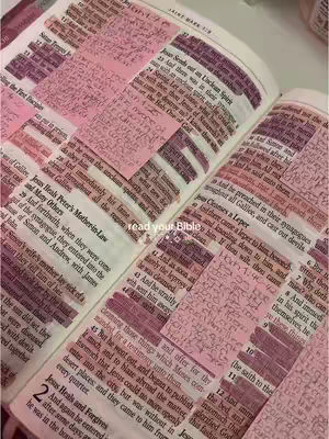 An open Bible with several pink sticky notes attached, each containing handwritten notes. The pages are yellowed, suggesting age, and the text is small and densely packed. The overall composition is framed from a top-down perspective, highlighting the content and annotations. The image palette leans towards muted tones of pink, beige, and brown.