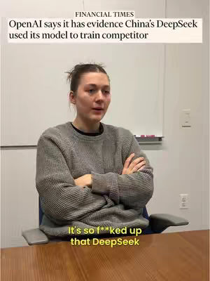 A woman with her arms crossed, seated in a room, likely an office. The background includes a whiteboard and neutral-toned walls. Overlaying text provides additional context.