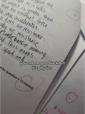 The image shows a close-up of a handwritten physics test on a white sheet of paper, with some areas circled and marked up with red ink. Text overlays such as "you tell me good luck but it's physics" add context, suggesting the difficulty of the subject.