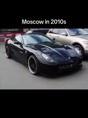 A black sports car is parked on a light gray surface with another car in the background. The sky is dark. Text overlay at the top says "Moscow in 2010s."
