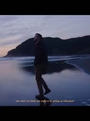 A man walks on a beach, with water in the foreground and cliffs in the background under a cloudy sky. Text is overlaid on the image.