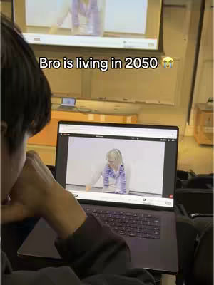 The cover image shows a person looking at a laptop screen in a room that looks like a lecture hall or classroom. The laptop displays a video feed, which is also visible on a large screen in the background. The text overlay reads 'Bro is living in 2050 😭'.