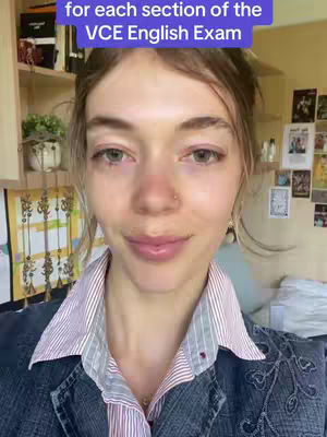 A close-up shot of a young woman in front of a cluttered background comprising bookshelves, papers, and a plant. The woman is wearing a denim jacket over a striped collared shirt with a small necklace and a nose piercing and is looking and smiling at the camera.