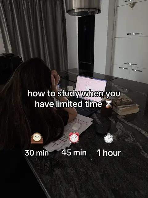 A person is seated at a dark countertop, presumably in a kitchen, with a laptop open in front of them. The person's back is to the camera, with their head resting on their hand. On the counter are papers, a pen, and a timer. White text overlays the image, detailing how to study with limited time, with time indicators using clock icons. The background shows white kitchen cabinets and dark curtains.