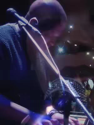 A person is holding a microphone, likely singing, against a dark background with stage lights.
