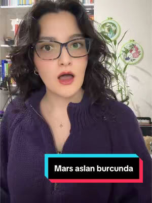 A woman in glasses with dark hair and a purple sweater is looking at the camera with her mouth open, as though she is about to speak. The background includes a bookshelf and some decorative items. The text "Mars aslan burcunda" is displayed in a black rectangle under the woman.