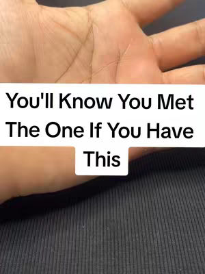 The image shows a close-up of a light-skinned hand with visible palm lines. Overlaid on the image is text in a white rectangle that reads: "You'll Know You Met The One If You Have This". The background appears to be a dark, textured surface.