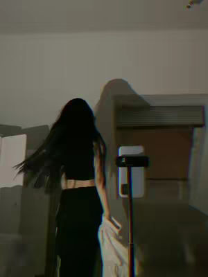 The cover image shows a person with long, dark hair, seen from behind, dancing or moving in a way that makes their hair fly. They are wearing a black outfit, a cropped top, or a sports bra showing the skin and high-waisted pants with a white stripe, or is a black bodysuit. The camera is focused on the back of the person. In the background, there's a stand for a phone used for filming. The overall tone of the image is casual. The picture is lit by studio lights inside a room.