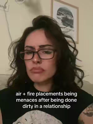 The cover image features a woman with glasses, looking directly at the camera with a slightly disapproving or serious expression. Text overlayed at the bottom reads, \"air + fire placements being menaces after being done dirty in a relationship\". The background is a plain wall with a framed artwork.