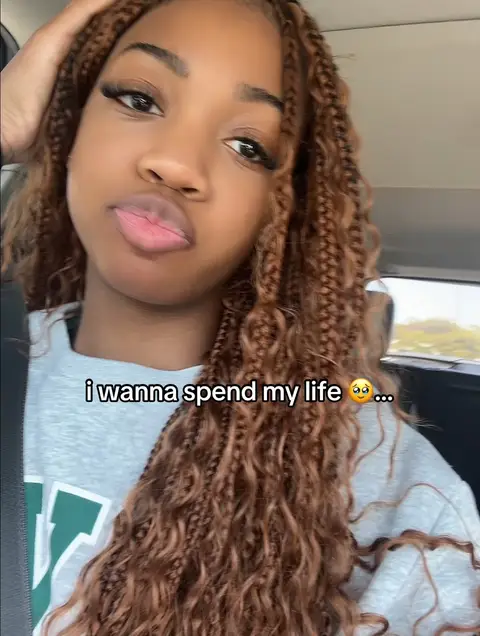 A selfie of a young woman in a car. She has brown braids, dark eyebrows and eyelashes, and is wearing a gray sweatshirt. She is holding her hand up to her head and has text overlaid on the image.