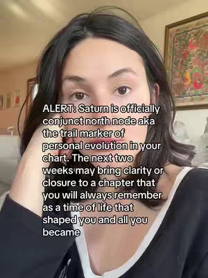 A woman with dark hair and a dark top is centered in the frame, with text overlayed. The background has framed pictures and the lighting appears to be soft and natural.