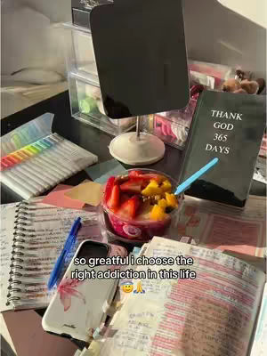The image shows a desk scene with a Bible, a fruit bowl, notebooks, and colorful markers. The text overlay on the image reads, 'so grateful I choose the right addiction in this life'. The composition suggests a focus on faith and healthy habits.