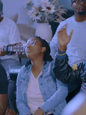 The cover image features a medium shot of a group of people, with a woman in the center noticeably raising her hands in worship. She wears glasses, a denim jacket, and a white shirt. Other individuals, including a person playing a keyboard, are blurred in the background.