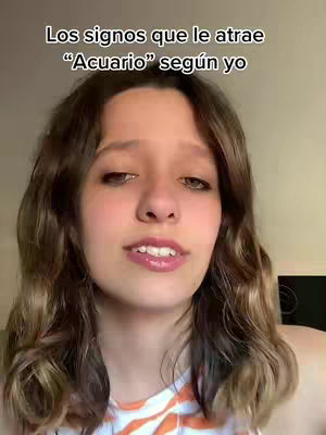 A young woman with wavy brown hair presents in a selfie-style video, with text overlay at the top. She is centered in the frame, looking up slightly with a subtle smile, wearing a white and orange patterned top, likely at home with a neutral backdrop. The lighting seems natural, enhancing the warm tones of her hair for a friendly presentation.