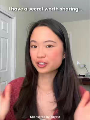 A woman with long dark hair and a red sweater is the main subject, framed from the chest up. She is looking toward the viewer, with a slightly opened mouth. The background shows a white door and a portion of a room that includes a desk and a lamp. The phrase "I have a secret worth sharing…" is written at the top of the frame, while the words "Sponsored by Toyota" are visible at the bottom.