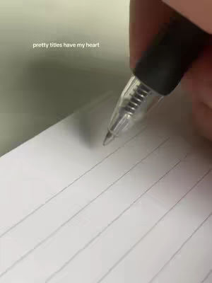 A hand holding a pen is positioned above a lined notepad, ready to write. The image is brightly lit, with the pen and the top of the hand visible.