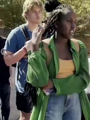 The cover image presents two individuals in what appears to be an outdoor setting. A person with dark skin, wearing a yellow top and green jacket, is the focus, gesturing with a hand and appears to speak. Behind them, a fair-skinned man in a blue t-shirt looks on. The background shows trees, hinting it's an outdoor location.