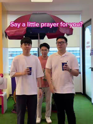 Three men are standing indoors, likely in an office or commercial space. A large, red and black umbrella-shaped structure hangs above them. The men are holding cups, with a green carpeted area in front of them, and a sign that says 'pizza square' appears in the visible background.