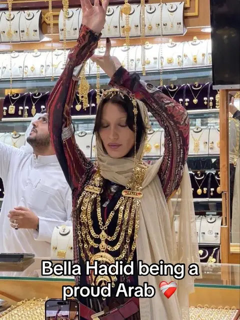 The cover image shows Bella Hadid in what appears to be a jewelry store, surrounded by gold necklaces and other adornments. She is dressed in an elaborate outfit with a head covering. Text overlayed says "Bella Hadid being a proud Arab." There's a phone at the bottom showing a recording.