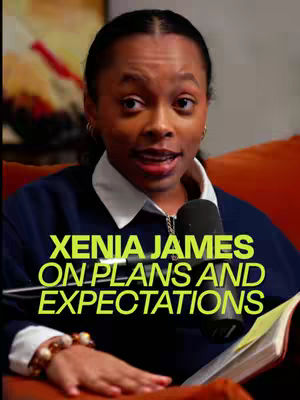 A woman with dark skin sits facing the viewer, lit from the front. She is wearing a dark blue sweater over a white collared shirt. Her black hair is styled back. Her brown eyes look directy at the viewer and her lips are slightly open. She has a microphone and a book or tablet in front of her. The background is blurry but shows tones of red and yellow. Text in yellow letters is overlaid on the image, identifying her name and the topic of the podcast.