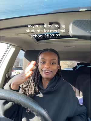 A woman with long dreadlocks is inside of a car, appearing to be the driver. She has a black hoodie on, and is waving. The text overlay is light-colored on the top of her head, inside of the car.