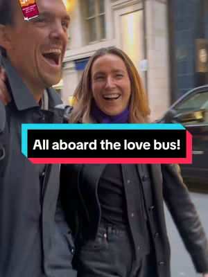 The cover image shows a cheerful couple walking down a city street. The man, on the left, has an arm around the woman, both smiling widely. They appear to be laughing. The image is slightly blurred, suggesting motion, and there's an overlay of text that reads, 'All aboard the love bus!' The overall tone is lighthearted and fun.