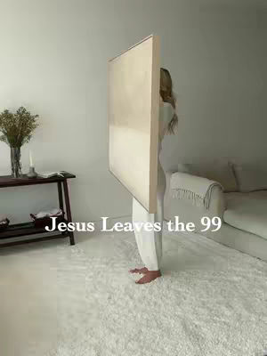 The image features a woman standing in a bright, minimalist room. She is partially obscured by a large, rectangular canvas, which she is holding in front of herself. The canvas is neutral-toned, with a gradient of light beige and white. The woman is dressed in matching white or beige attire, blending subtly with the background. The room has a clean, modern aesthetic, highlighted by a white rug. A small table with a still-life arrangement and a sofa can be seen in the background. The text "Jesus Leaves the 99" is overlaid at the bottom of the image.
